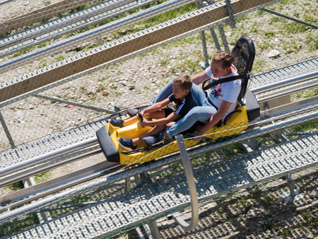 Russia, Sochi 04.08.2019. The elder brother and younger brother ride their hair at high speed back on Rodelbahn. Rosa Khutor. Height 1100 metersのeditorial素材