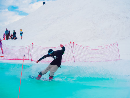 Russia, Sochi 11.05.2019. A guy rider at high speed crosses a pool of birch-colored water. Snowboard competition on the water in the Krasnaya Polyana ski resort.のeditorial素材