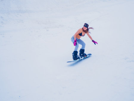 Russia, Sochi 11.05.2019. A beautiful girl in a swimsuit with a go pro camera on her head is quickly riding a snowboard down the slope. Krasnaya Polyanaのeditorial素材