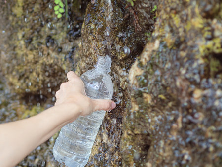 A womans hand fills a plastic bottle with spring water from a spring flowing down the rock. Maidens...