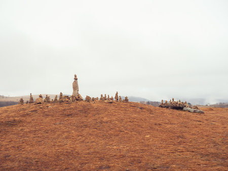 Many stone pyramids are built on top of the mountain covered with dry grass against the background of white thick clouds. Caucasian Highlandsの写真素材