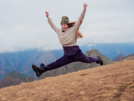 A woman jumps a twine over an autumn field in the highlands of a mountain valley against the...