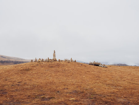 Many stone pyramids are built on the top of a mountain covered with dry grass against the backdrop of thick white clouds.の写真素材