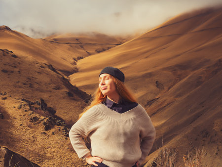 High in the mountains of the Caucasus where the clouds lie on the peaks, a smiling tourist stands and enjoys the autumn natureの写真素材