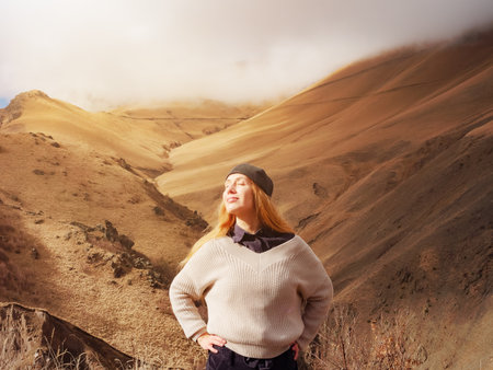 High in the mountains of the Caucasus, where the clouds lie on the peaks, a smiling tourist stands and enjoys the autumn sun peeking out from behind the clouds.の写真素材
