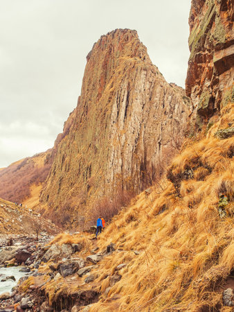 Travelers walk along a mountain river in the distance against the backdrop of a tall steep cliff. Country autumn landscape of the Caucasusの写真素材