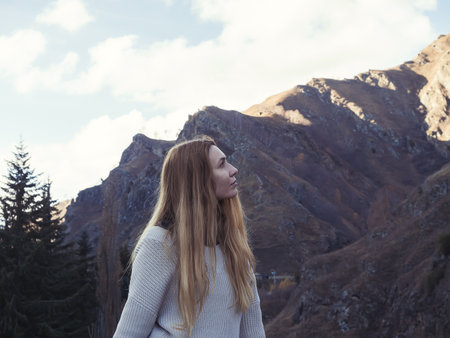 Profile of a woman against the backdrop of steep Caucasian mountains and trees on an autumn day.の写真素材