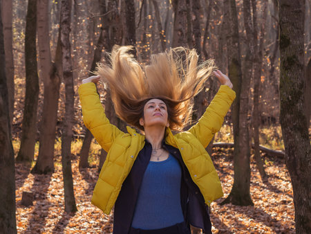 A woman throws back her long hair while standing in the autumn forest among the fallen leaves on a sunny autumn dayの写真素材