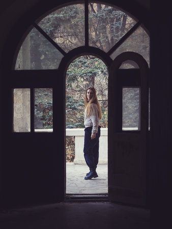 View through the doorway of a woman standing on the balcony of an old empty and dark abandoned building located in the forestの写真素材