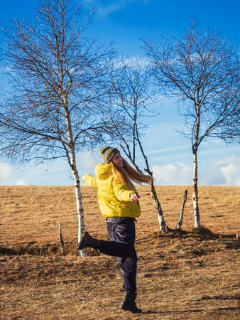 Laughing woman in a yellow jacket jumps on an autumn field against a blue sky on a sunny day.の写真素材