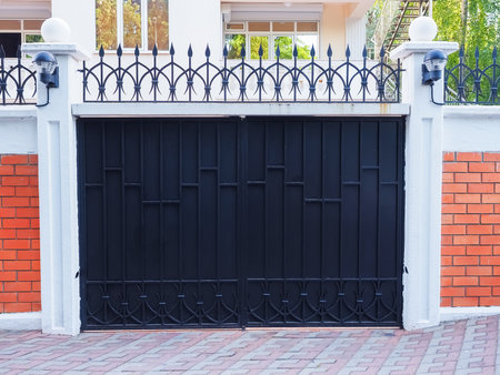 Iron black gate with a wrought pattern and sharp tips at the top and with a brick fence. Protected...