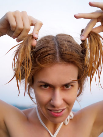 A funny girl with a stern look holds her wet pigtails. Summer sea holidays.の写真素材