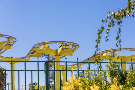 The yellow zigzag attraction is visible from behind the forged fence and green foliage on a clear...