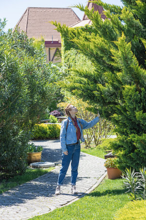 A woman in a denim outfit walks along a paved path admiring the park trees on a sunny spring day.の写真素材