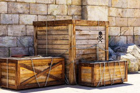 Wooden boxes with the image of a skull and crossbones wrapped in chains stand against the backdrop of a stone wall. Pirate treasure. Amusement park decorの写真素材