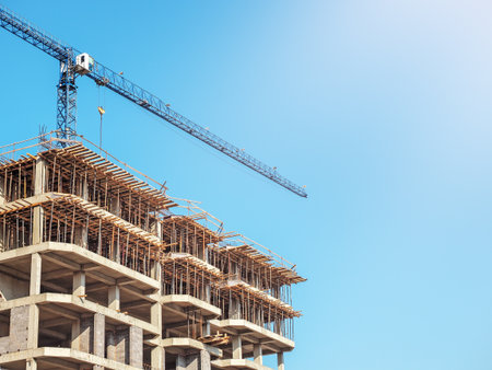 Crane building a house on the sky background. A crane rises above a building under construction against a blue sky on a sunny clear dayの写真素材