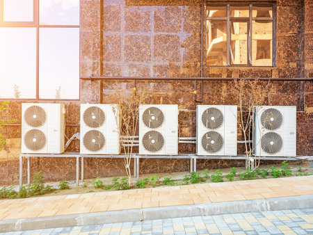 Many air conditioners on the wall. A row of double industrial air conditioners is mounted on a brown marble tiled wall. View outside.の写真素材
