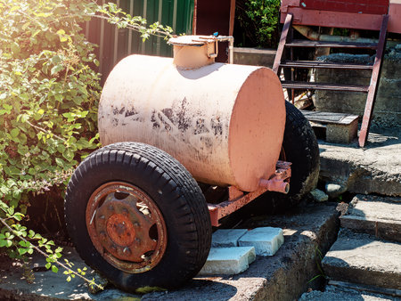 Water tank trailer on wheels. Barrel on wheels. A light pink rusting iron tank on wheels stands in the countryside on concrete slabs. Water tank.の写真素材