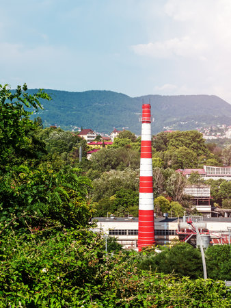 Red and white chimney of a boiler house. City industrial zone. Cityscape in green hills.の写真素材