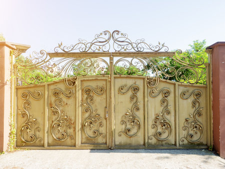 Rusting gate with forged pattern. Iron gate with wrought iron pattern. Beige iron gate with wrought iron pattern and rust stains on a summer sunny day. Abandoned private areaの写真素材
