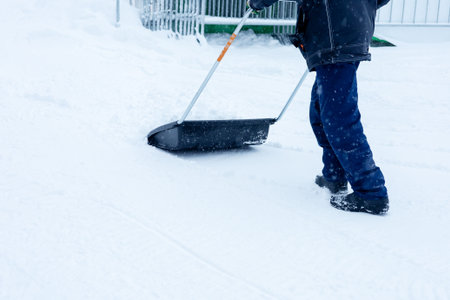 Legs of a janitor removing snow with a shovel. Clearing snow drifts on a winter dayの写真素材