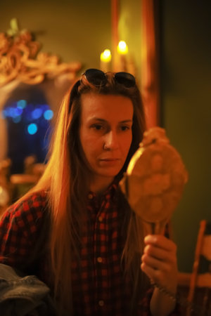 Woman looks in the mirror by candlelight. Portrait of a woman divining by candlelight. Modern woman with vintage interior. Blurred imageの写真素材