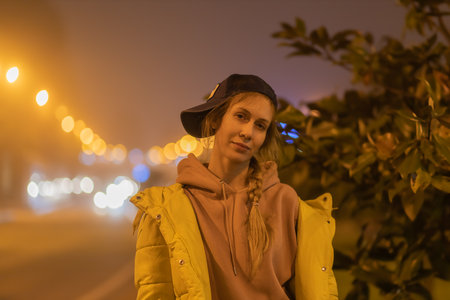 Portrait of a woman against the backdrop of a night glowing foggy city. A woman stands in the night city in the light of lanternsの写真素材