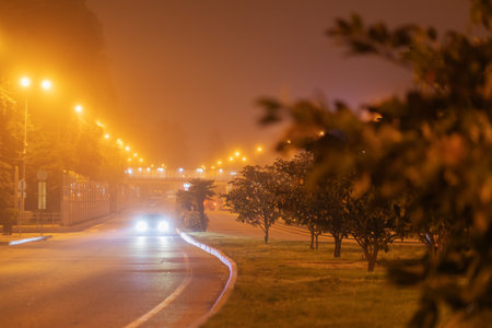 Glowing city road on foggy night. A car with glowing headlights is driving along a night road in the fog. Blurred imageの写真素材
