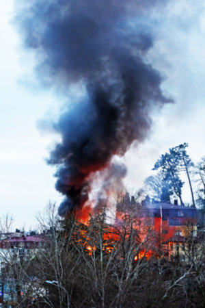 Strong fire. The house is on fire behind the trees. Strong fire and black column of smoke. Blurred...