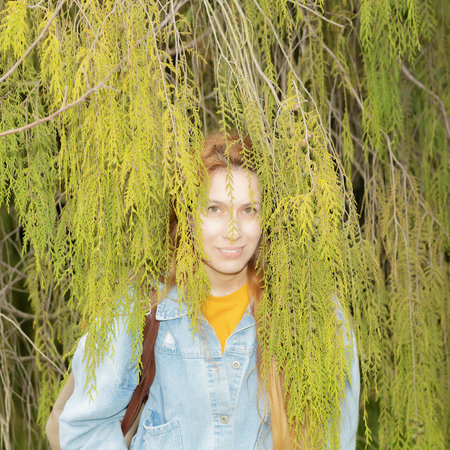 Woman peeking out from behind cypress branches. Disguise in the branches of a tree. Selective focus.の写真素材