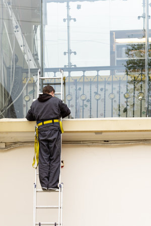 An electrician on a ladder performs work. Worker in work clothes on stairsの写真素材