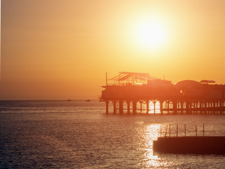Silhouette of a building on a pier in a calm sea at sunset. Construction on the pier in the sea at sunset. Cafe on the pier at sunset. Blurred imageの写真素材