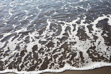 The gentle white foam of the sea spreads onto the sandy shore, creating intricate patterns on the...