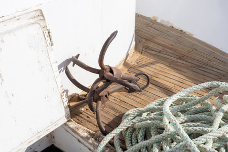 A vintage nautical anchor rests alongside coiled rope on a weathered wooden deck, evoking maritime history and adventure. the sunlight highlights the contrast between the rustic iron and the worn texture of the wood. ideal for themes of nautical exploration and coastal living, this image enduring essence of sea travel and craftsmanship.の写真素材