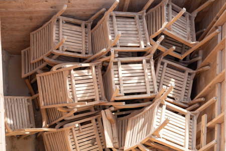 A rustic scene featuring wooden chairs neatly stacked in a sunlit storage area. the natural wood tones and textures create a cozy and inviting ambiance, ideal for outdoor seating arrangements. perfect for design inspiration related to casual and minimalist spaces, capturing simplicity and warmth.の写真素材