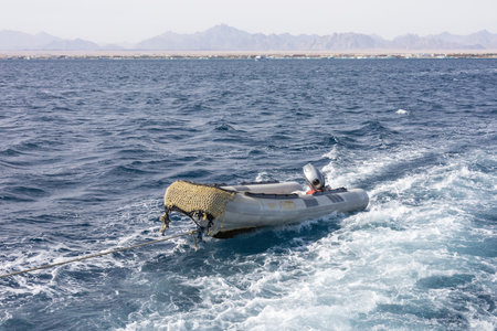 A tranquil scene of an inflatable dinghy sailing across the deep blue sea with distant mountains in...