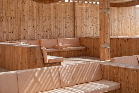 This image features a cozy outdoor seating area with rustic wooden benches bathed in natural light. the warm tones and serene atmosphere create a relaxing environment. perfect for designs focused on architecture, outdoor living, or inviting retreat spaces. the play of shadows adds depth and interest to the minimalist layout.の写真素材