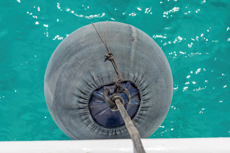 Close-up image of a boat fender floating on vibrant turquoise water, showing its role in maritime safety. the scene juxtaposition of the fenders texture against the shimmering blue surface. ideal for themes of sea travel, nautical adventures, and coastal leisure. perfect for use in designs related to marine activities and summer exploration.の写真素材