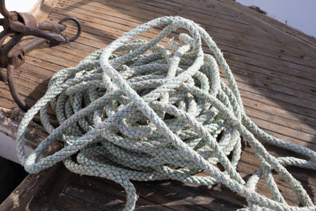 Nautical scene featuring a coiled rope on a weathered wooden deck, exuding a maritime atmosphere. the ropes texture and intricate pattern are highlighted by sunlight, adding depth to this rugged seafaring image. ideal for themes of adventure, boating, and coastal exploration.の写真素材