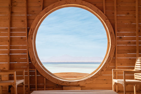 A tranquil indoor setting featuring a large circular window offering a breathtaking view of the serene sea and distant mountains. the wooden architecture adds warmth and simplicity, creating a peaceful atmosphere perfect for relaxation and reflection. ideal for designs emphasizing natural beauty and open spaces.の写真素材