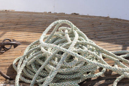 A detailed image of a coiled nautical rope on a weathered wooden deck, evoking maritime charm and adventure. the natural texture and braided pattern highlight traditional seafaring elements, perfect for themes of sailing and coastal living. the rustic appeal makes it suitable for marine-themed decor or storytelling.の写真素材