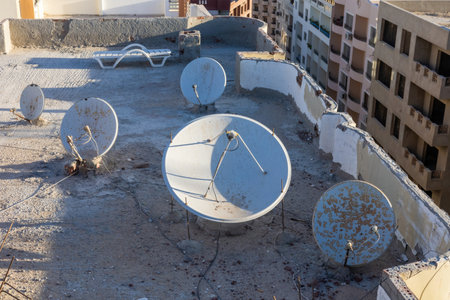 An urban rooftop scene featuring multiple satellite dishes against a sunset backdrop, the blend of technology and architecture in cityscapes. the concrete surface shows signs of wear, adding a rustic charm to modern communication structures. ideal for themes of urbanization, technology, and broadcasting.の写真素材