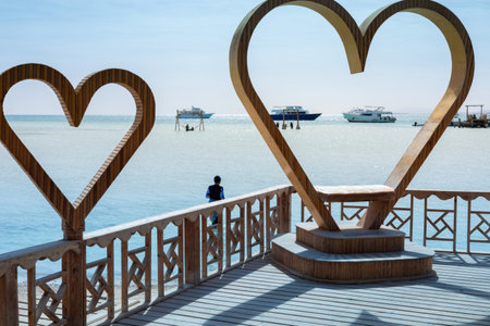 A captivating scene featuring large wooden heart sculptures on a deck overlooking a serene ocean horizon. the tranquil view includes distant boats under a bright blue sky, creating a romantic and peaceful atmosphere. perfect for themes of travel, romance, or summer escape, the image conveys relaxation and inspiration. ideal for vacation promotions or decorative designs.の写真素材