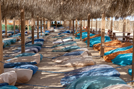 A scenic view of a relaxing outdoor seating area under a thatched roof, featuring colorful cushions on sandy ground. the arrangement offers a tranquil atmosphere, ideal for a tropical escape or summer retreat. sunlight filters through, creating a warm and inviting setting perfect for leisure and relaxation.の写真素材