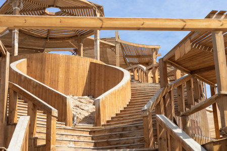 Captivating image of a rustic wooden staircase ascending to a pavilion, under a clear blue sky. The intricate woodwork and natural textures create a serene and inviting atmosphere, perfect for architectural design or travel inspiration. The interplay of sunlight and shadows highlights the craftsmanship and earthy ambiance. Ideal for applications emphasizing outdoor design and natural beauty.の写真素材
