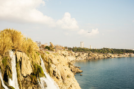 Scenic view of coastal cliffs and waterfall with city skyline in the distance.の写真素材