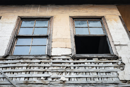 Weathered old building with broken windows and worn wooden lattice on rustic wall.の写真素材