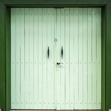 Pale green wooden door with iron handles on rustic frame.の写真素材