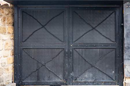 Rustic black metal gate with stone wall backdrop.