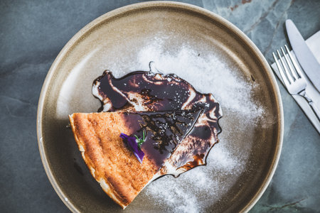 Delicious cheesecake slice with chocolate sauce and sugar on a plate.の写真素材